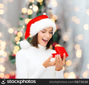 winter, happiness, holidays and people concept - smiling woman in santa helper hat with gift box over living room and christmas tree background