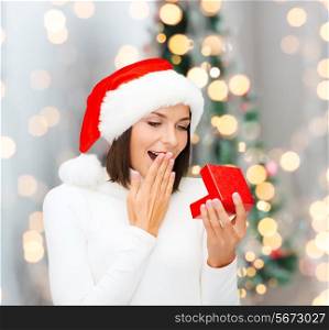winter, happiness, holidays and people concept - smiling woman in santa helper hat with gift box over living room and christmas tree background
