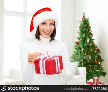 winter, happiness, holidays and people concept - smiling woman in santa helper hat with gift box over living room with christmas tree background