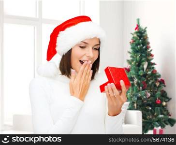 winter, happiness, holidays and people concept - smiling woman in santa helper hat with gift box over living room and christmas tree background