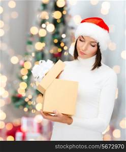 winter, happiness, holidays and people concept - woman in santa helper hat with gift box over living room and christmas tree background