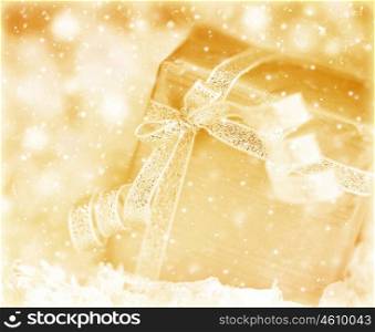Winter holiday background with golden present gift box, beautiful shiny ribbon ornament &amp; Christmas snow decoration