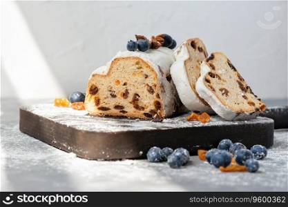 Winter holiday sweet dessert with raisins, blueberry and sugar powder icing. Lifestyle traditional Christmas stollen, sliced on a pieces on wooden board, in sunlight.. Winter holiday sweet dessert with raisins, blueberry and sugar powder icing. Lifestyle traditional Christmas stollen, sliced on pieces on wooden board, in sunlight.