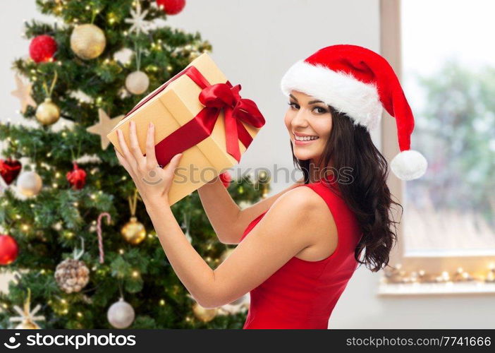 winter holidays and celebration concept - beautiful woman in red dress with gift box over christmas tree at home on background. beautiful woman in red dress with christmas gift