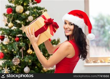 winter holidays and celebration concept - beautiful woman in red dress with gift box over christmas tree at home on background. beautiful woman in red dress with christmas gift