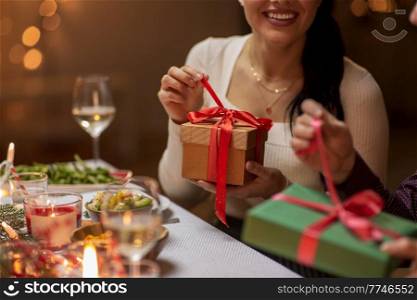 winter holidays and celebration concept - close up of happy smiling people opening christmas gifts at home dinner party. happy people with christmas gifts at dinner party
