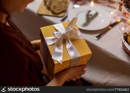 winter holidays and celebration concept - close up of happy woman opening christmas gifts at home dinner party. happy woman opening christmas gift at dinner party