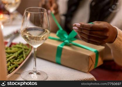 winter holidays and celebration concept - close up of woman opening christmas gifts at home dinner party. woman opening christmas gift at dinner party