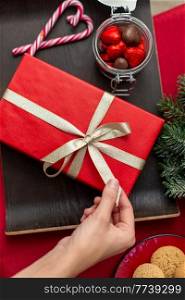 winter holidays and celebration concept - hand with christmas gift, treats and decorations on table at home. hand with christmas gift, treats and decorations