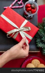 winter holidays and celebration concept - hand with christmas gift, treats and decorations on table at home. hand with christmas gift, treats and decorations