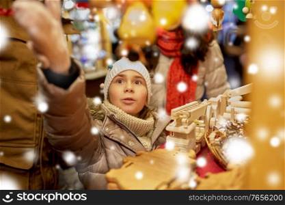winter holidays and celebration concept - happy girl with family choosing souvenirs at christmas market on town hall square in tallinn, estonia over snow. happy family buying souvenirs at christmas market