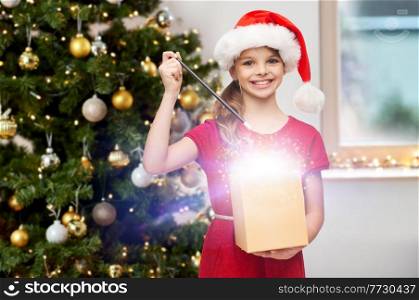 winter holidays and celebration concept - happy smiling girl with magic wand and gift box with fairy dust at home over christmas tree background. smiling girl with magic wand and christmas gift