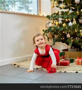 winter holidays and childhood concept - happy baby girl christmas tree and gifts at home. happy baby girl with christmas gifts at home