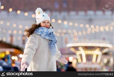 winter holidays and children concept - portrait of happy little girl over christmas market amusement park background. happy little girl at christmas amusement park