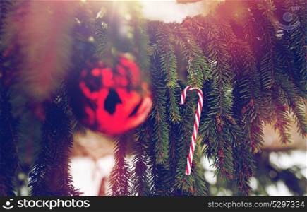 winter holidays and decoration concept - candy cane and christmas ball on fir tree branch covered with snow. candy cane and christmas ball on fir tree branch