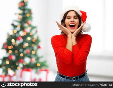 winter holidays and emotions concept - happy smiling young woman in santa helper hat over christmas tree lights background. happy young woman in santa hat on christmas