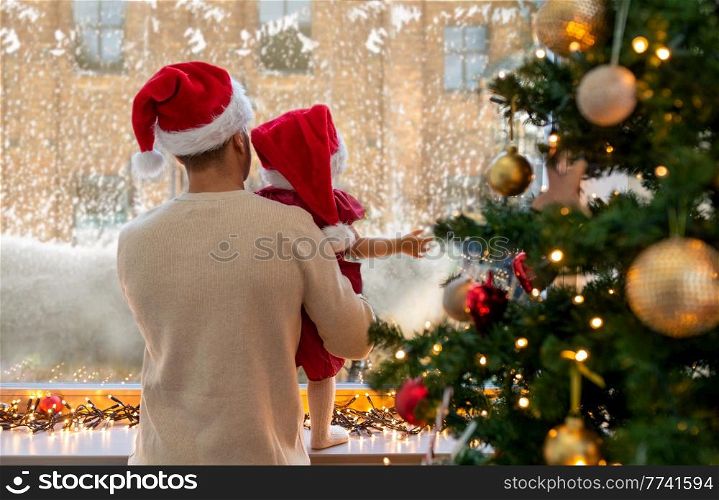 winter holidays and family concept - father and baby daughter looking through window on christmas at home. father and baby daughter on christmas at home