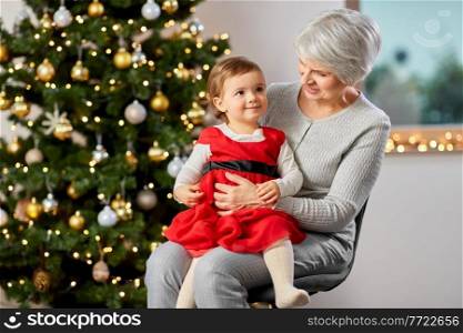 winter holidays and family concept - happy grandmother and baby granddaughter at christmas tree. grandmother and baby girl with at christmas tree