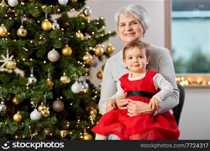 winter holidays and family concept - happy grandmother and baby granddaughter at christmas tree. grandmother and baby girl with at christmas tree