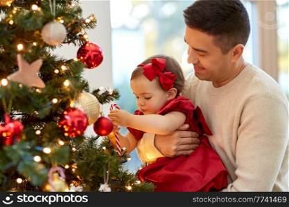 winter holidays and family concept - happy middle-aged father and baby daughter decorating christmas tree with toy candy cane at home. happy father and baby girl decorate christmas tree