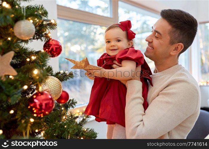 winter holidays and family concept - happy middle-aged father and baby daughter decorating christmas tree with star at home. happy father and baby girl decorate christmas tree