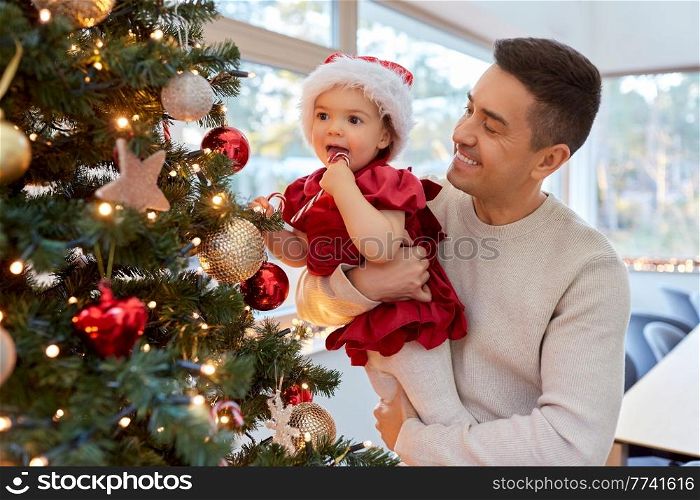 winter holidays and family concept - happy middle-aged father and baby daughter decorating christmas tree with toy candy cane at home. happy father and baby girl decorate christmas tree