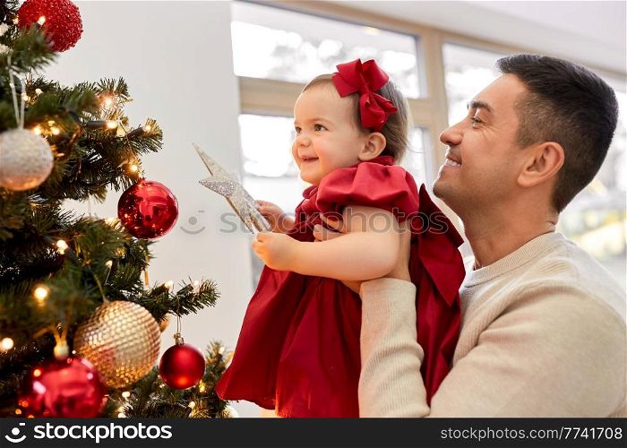 winter holidays and family concept - happy middle-aged father and baby daughter decorating christmas tree with star at home. happy father and baby girl decorate christmas tree