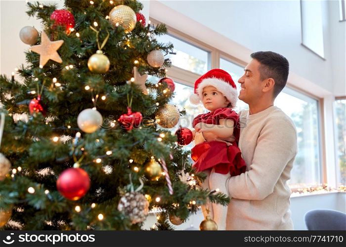 winter holidays and family concept - happy middle-aged father and baby daughter decorating christmas tree at home. happy father and baby girl decorate christmas tree