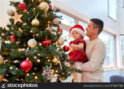 winter holidays and family concept - happy middle-aged father and baby daughter decorating christmas tree at home. happy father and baby girl decorate christmas tree
