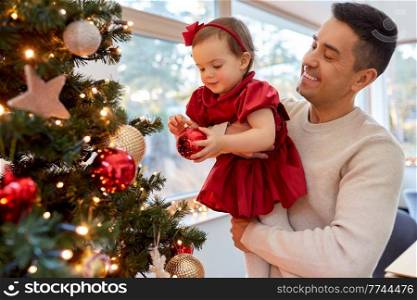 winter holidays and family concept - happy middle-aged father and baby daughter decorating christmas tree with ball at home. happy father and baby girl decorate christmas tree