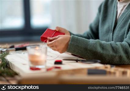 winter holidays and hobby concept - close up of woman with box and rope packing christmas gift or making advent calendar at home. close up of woman packing christmas gift at home
