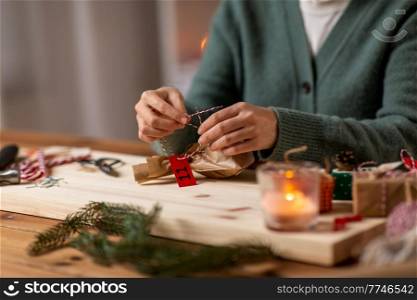 winter holidays and hobby concept - close up of woman with box and rope packing christmas gift or making advent calendar at home. woman making advent calendar on christmas at home