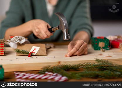 winter holidays and hobby concept - close up of woman with hammer hammering nails in wooden board and making advent calendar at home. woman making advent calendar on christmas at home