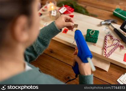 winter holidays and hobby concept - close up of woman with hot glue gun packing christmas gift or making advent calendar at home. woman making advent calendar on christmas at home
