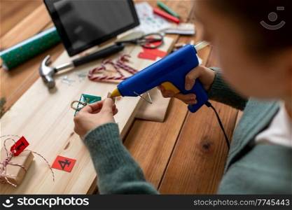 winter holidays and hobby concept - close up of woman with hot glue gun packing christmas gift or making advent calendar at home. woman making advent calendar on christmas at home