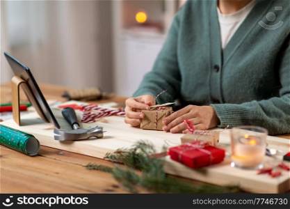 winter holidays and hobby concept - close up of woman with tablet pc computer packing christmas gift or making advent calendar at home. woman with tablet pc packing christmas gift