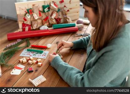 winter holidays and hobby concept - woman with clothespin and fir branch making advent calendar on christmas at home. woman making advent calendar on christmas at home