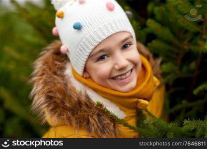 winter holidays and people concept - close up of happy smiling little girl choosing christmas tree at street market. little girl choosing christmas tree at market