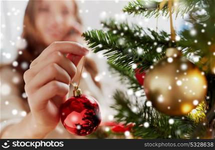 winter holidays and people concept - close up of young woman hand decorating christmas tree with red ball over snow. close up of woman hand decorating christmas tree