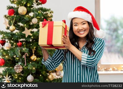 winter holidays and people concept - happy asian young woman with gift box over christmas tree on background. happy asian woman with birthday present