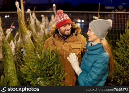 winter holidays and people concept - happy couple buying christmas tree at street market in evening. happy couple buying christmas tree at market
