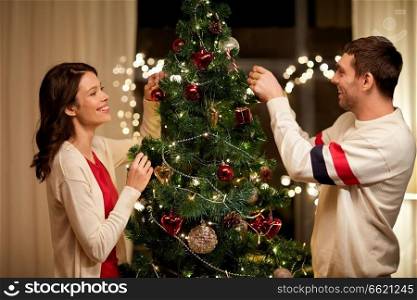 winter holidays and people concept - happy couple decorating christmas tree at home. happy couple decorating christmas tree at home