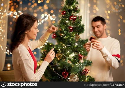 winter holidays and people concept - happy couple decorating christmas tree at home. happy couple decorating christmas tree at home