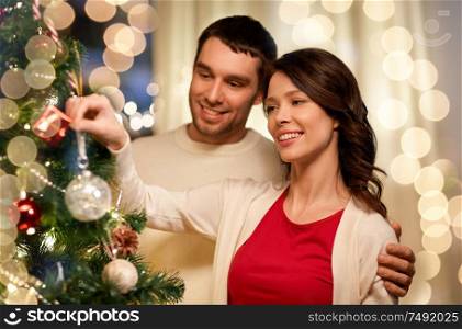 winter holidays and people concept - happy couple decorating christmas tree at home. happy couple decorating christmas tree at home