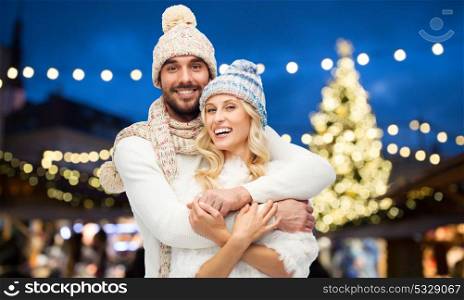 winter, holidays and people concept - happy couple in hats hugging over christmas tree lights background. happy couple hugging over christmas tree lights