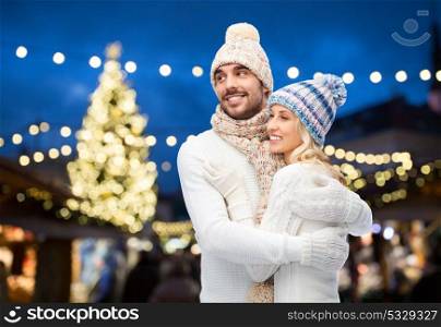 winter, holidays and people concept - happy couple in hats hugging over christmas tree lights background. happy couple hugging over christmas tree lights