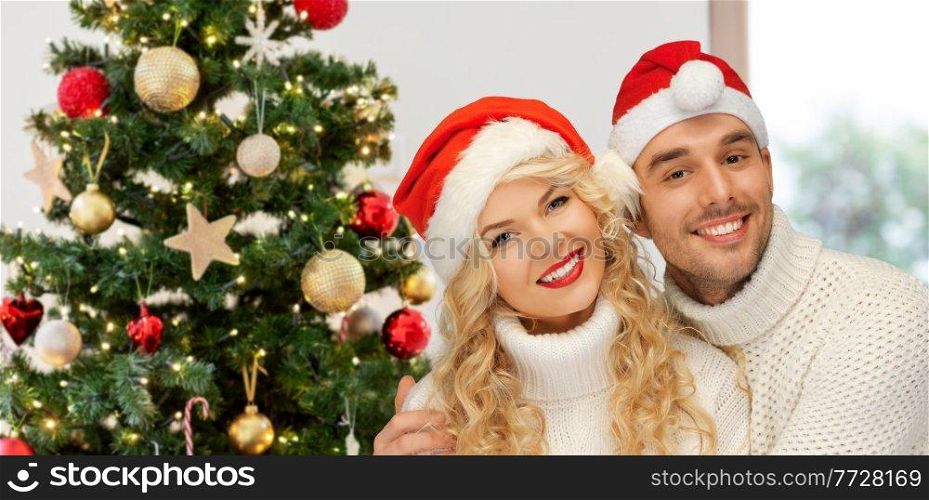 winter holidays and people concept - happy couple in sweaters and santa&rsquo;s hats over christmas tree lights on background. happy couple in santa&rsquo;s hats on christmas