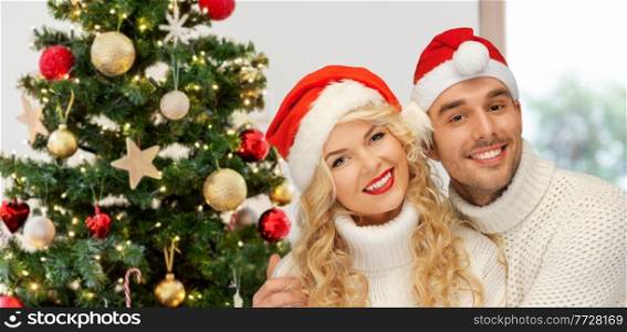 winter holidays and people concept - happy couple in sweaters and santa&rsquo;s hats over christmas tree lights on background. happy couple in santa&rsquo;s hats on christmas
