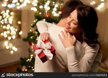 winter holidays and people concept - happy couple with christmas gift hugging at home. happy couple with christmas gift hugging at home