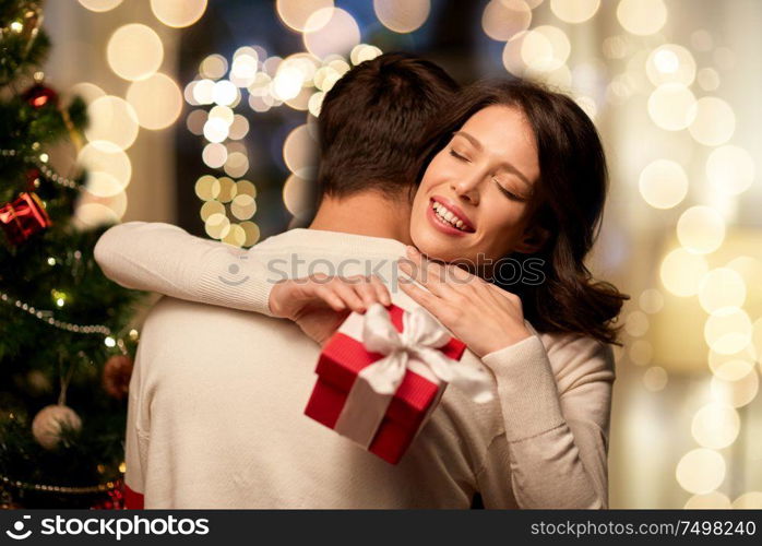 winter holidays and people concept - happy couple with christmas gift hugging at home. happy couple with christmas gift hugging at home